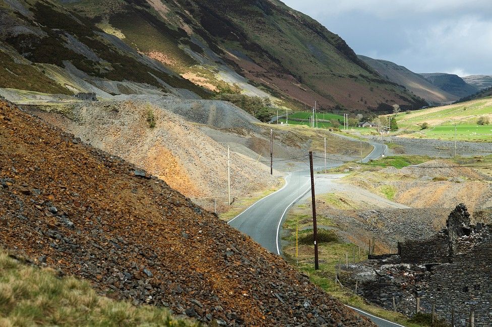 Piles of different coloured rubble and rock at the side of the road going through a valley