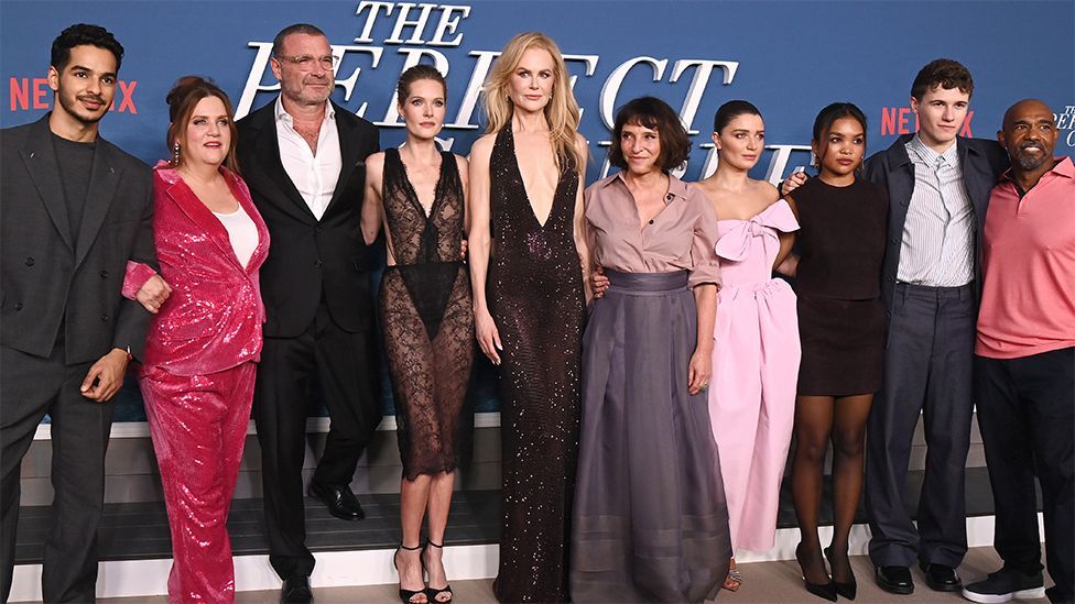 The cast of The Perfect Couple, from left to right, Ishaan Khatter, Donna Lynne Champlin, Liev Schreiber, Meghann Fahy, Nicole Kidman, Susanne Bier, Eve Hewson, Mia Isaac, Sam Nivola and Michael Beach. At the Los Angeles Premiere, with "The Perfect Couple" written in white on a blue background behind the cast.