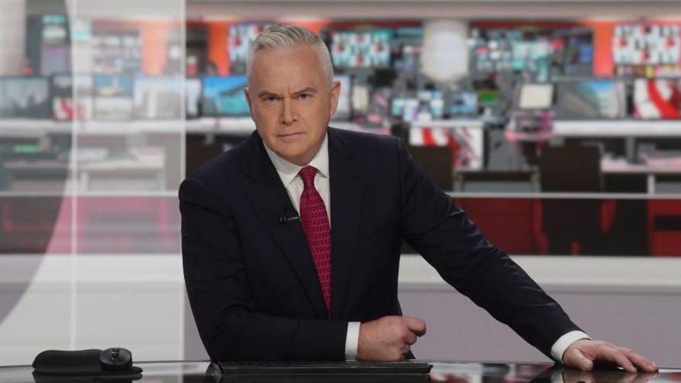 Huw Edwards presenting the news in studio wearing suit and red tie