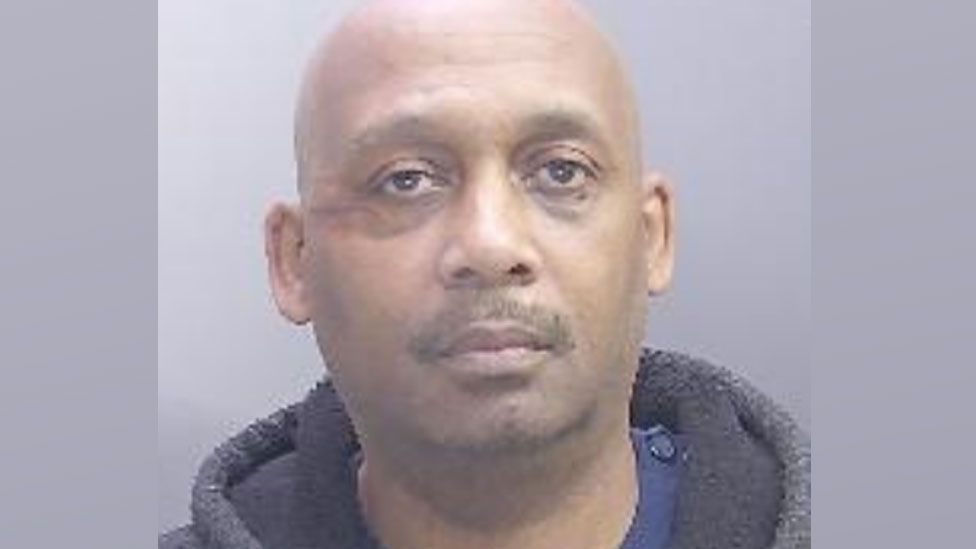 Ardley Ward's mugshot - he is a bald man with stubble wearing a grey fluffy hoody over a blue top, looking at the camera