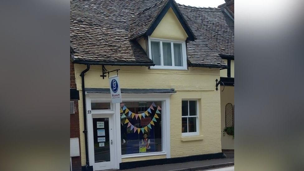 A light yellow building with a large window decorated with bunting