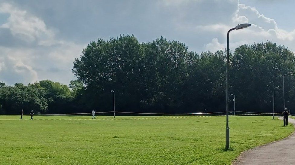 Northlands Park, in Basildon. A forensics officer can be seen on a field where cordon tape is in place. There are trees in the background.