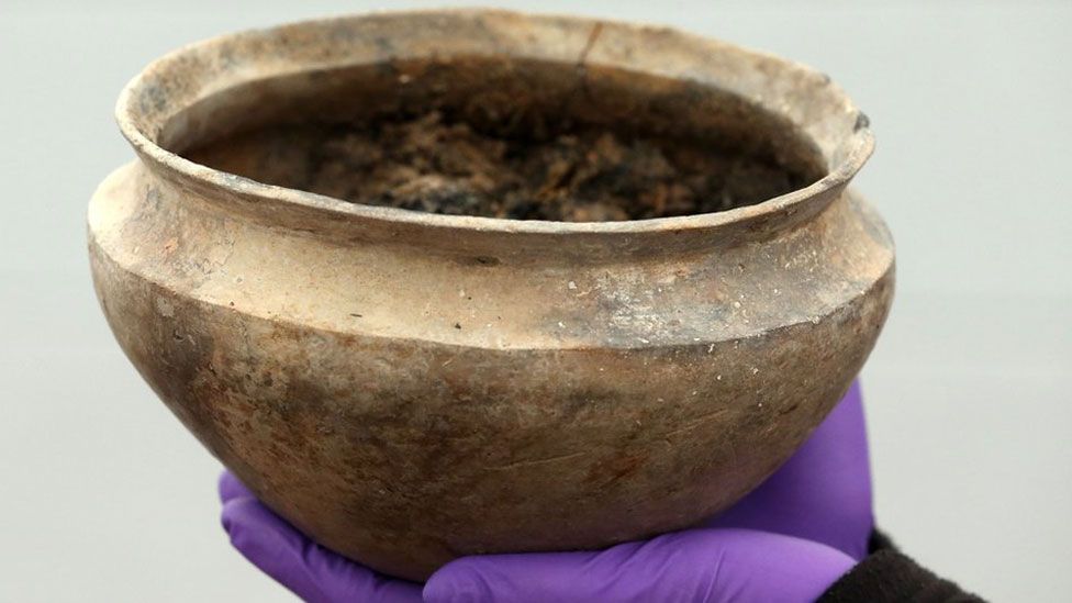 An intact Bronze Age pot held up towards the viewer in plastic-clad hands