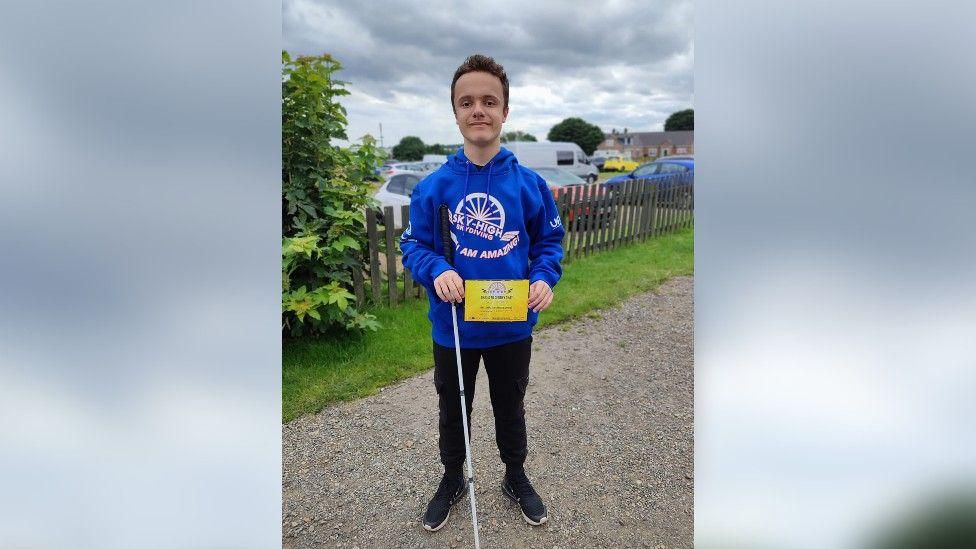 Jack, in a blue sweatshirt, holding a certificate to say he has completed the skydive