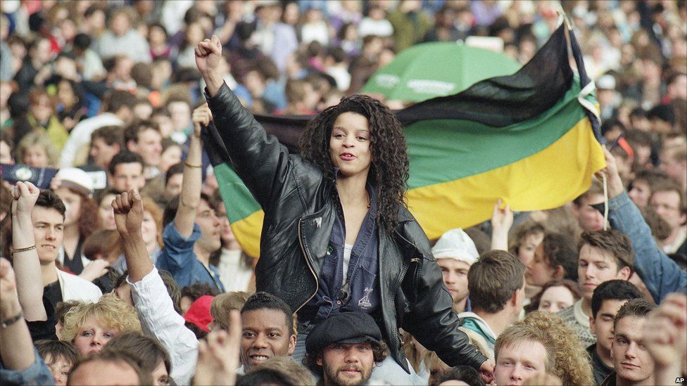 Music fans give the clenched fist and hold an African National Congress flag at Wembley Stadium, London, prior to the start of the Nelson Mandela Concert, April 16, 1990