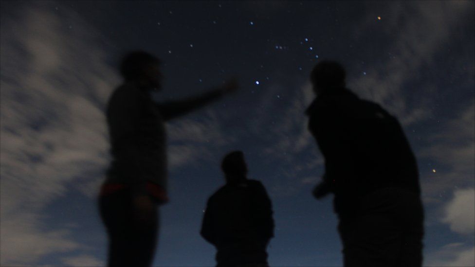 Figures standing and pointing at stars in the sky