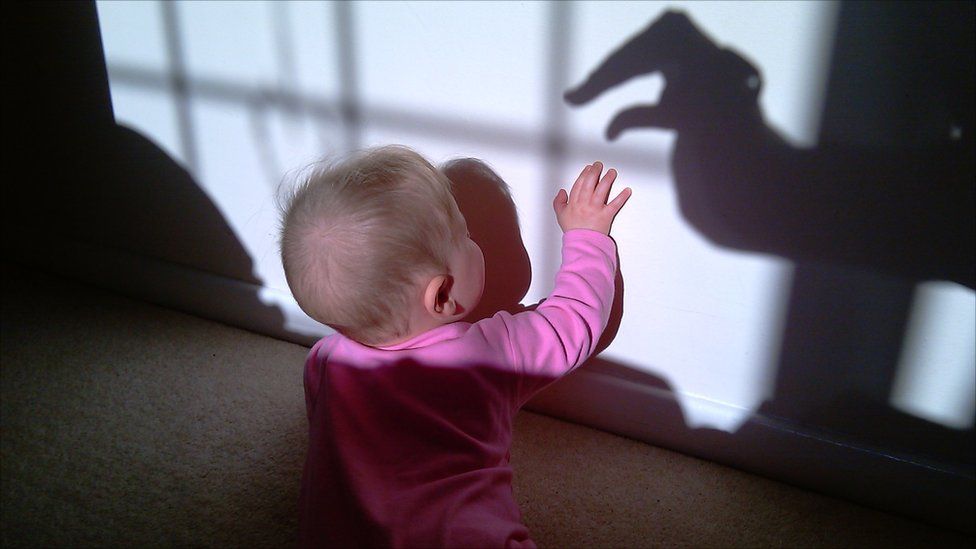 A baby tries to touch a shadow of a hand