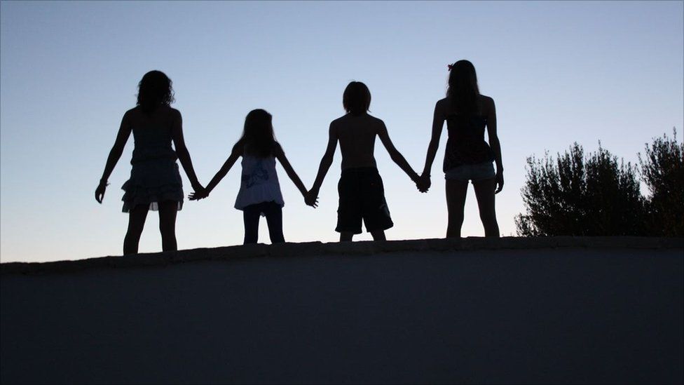 The silhouettes of four children holding hands in a line