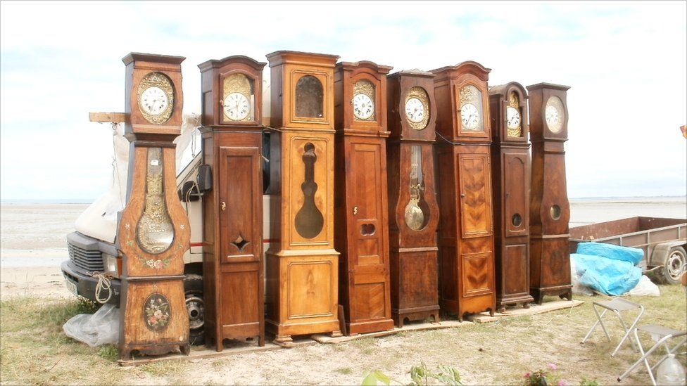 A row of grandfather clocks for sale at an outdoor market in France.