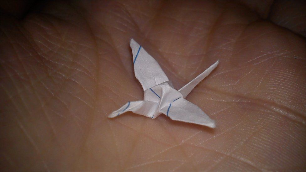 A small paper origami crane in the palm of a hand