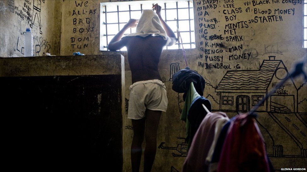 A prisoner stares out of his through bars from his cell where the walls are covered with graffiti - Liberia's Monrovia Central Prison, 2011