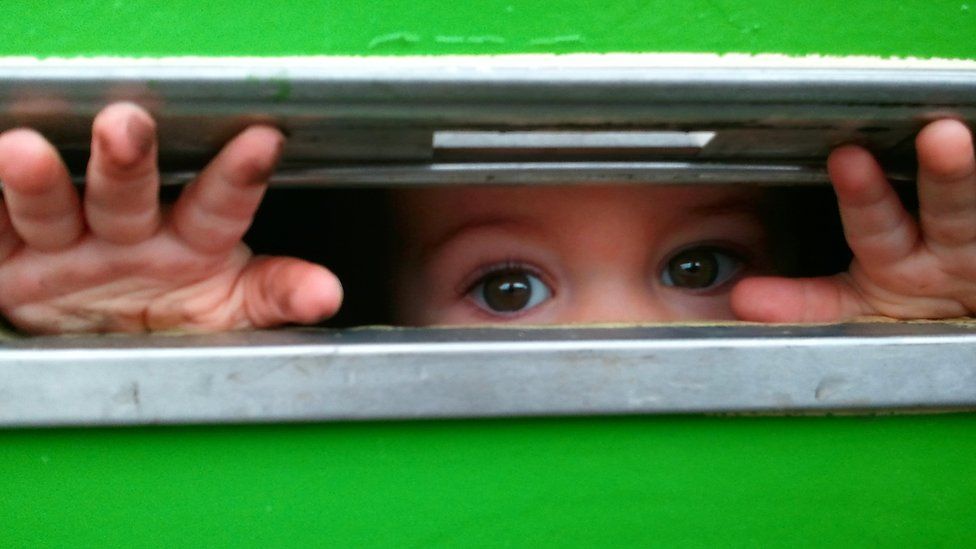A child peering through a letter box with grubby fingers