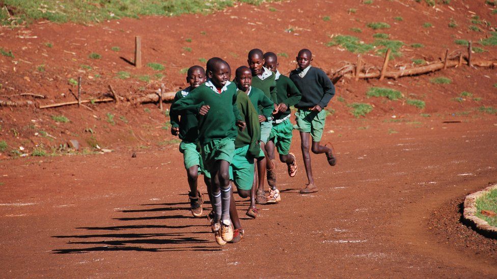 a photo of school children in Iten, where Abel Kirui trains, running around an athletics track after some full-time Kenyan athletes.