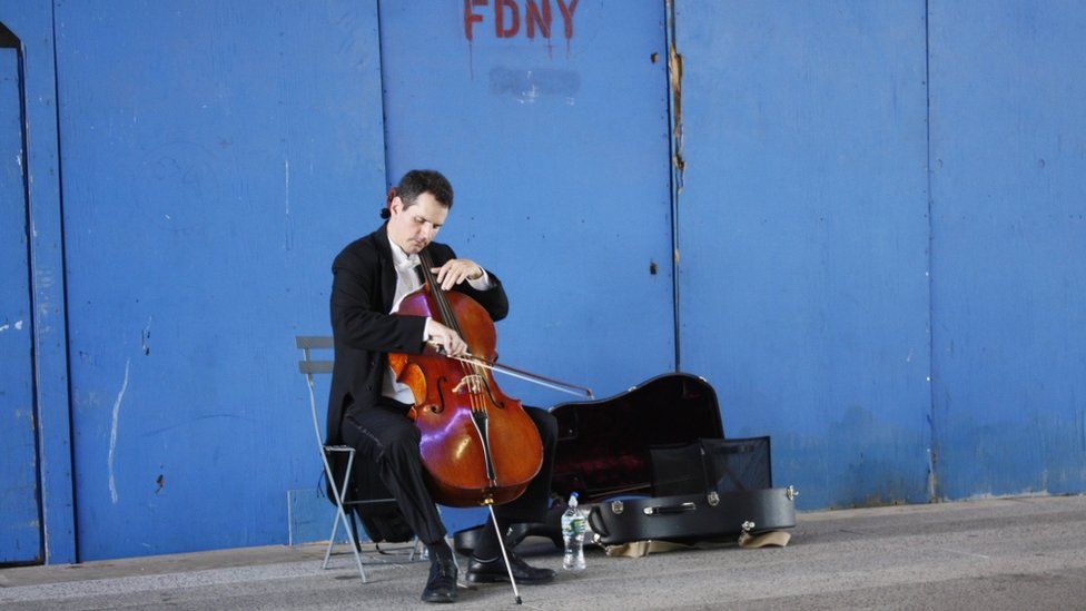 A man plying a cello in front of a blue wall