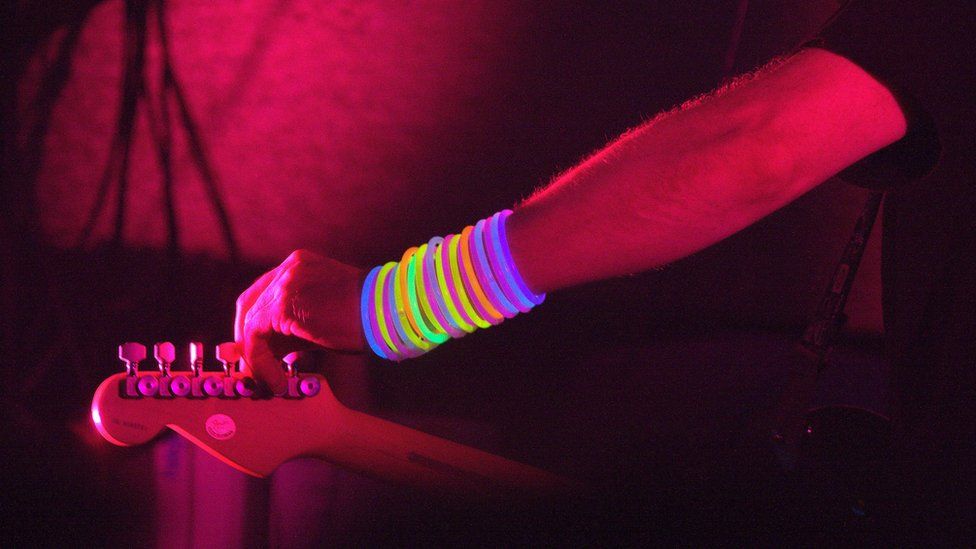 A guitarist with day glow wrist bands tunes his guitar