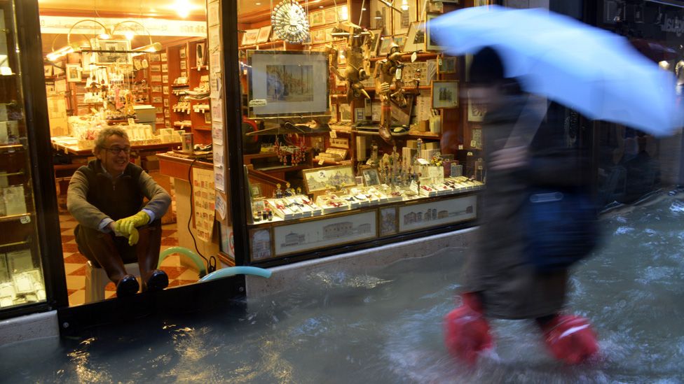 A man sits in his shop as a passer-by wades through a flooded street in Venice, 11 November 2012