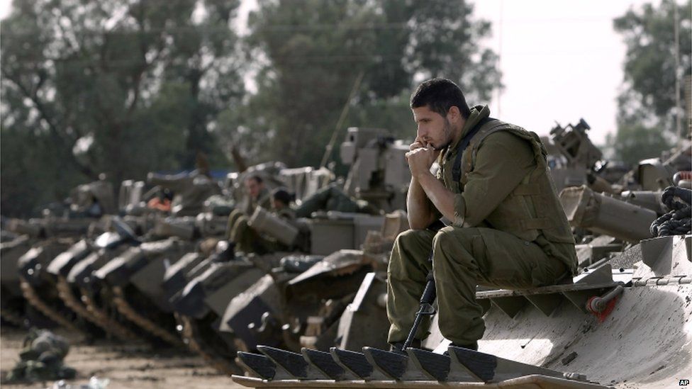 An Israeli soldier sits on the front of one of a line of armoured personnel carriers on the border with Gaza