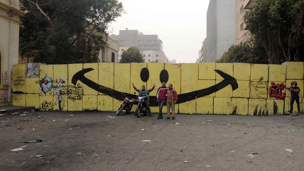 Men pose in front of graffiti on Qasr al-Aini Street, Cairo