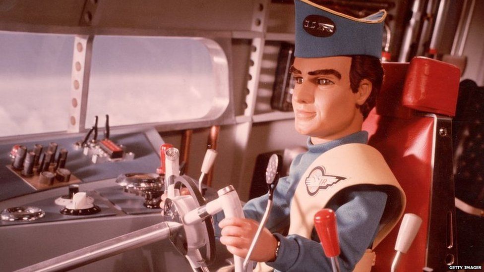 A marionette pilot in uniform steers a vehicle