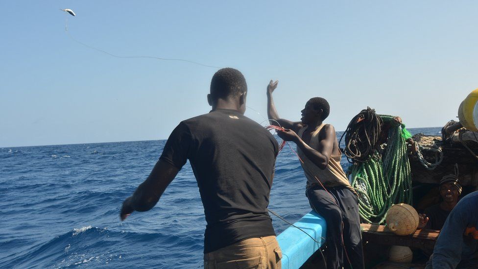 A crew member aboard the Kenyan fishing vessel throws a fish attached to a longline into the sea