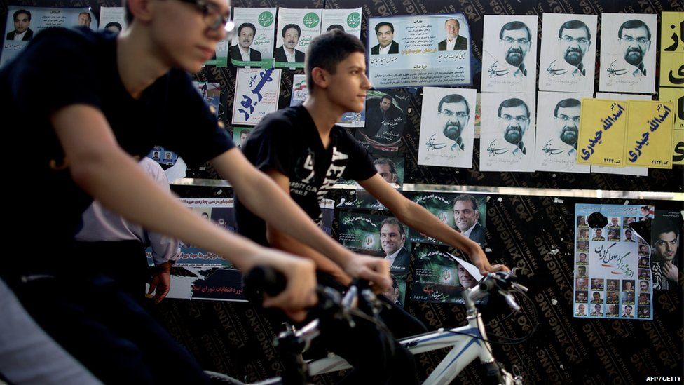 Iranian youths ride their bicycles past campaign posters of Mohsen Rezai, conservative presidential candidate and former chief of the Revolutionary Guards, and candidates for the municipality election in central Tehran