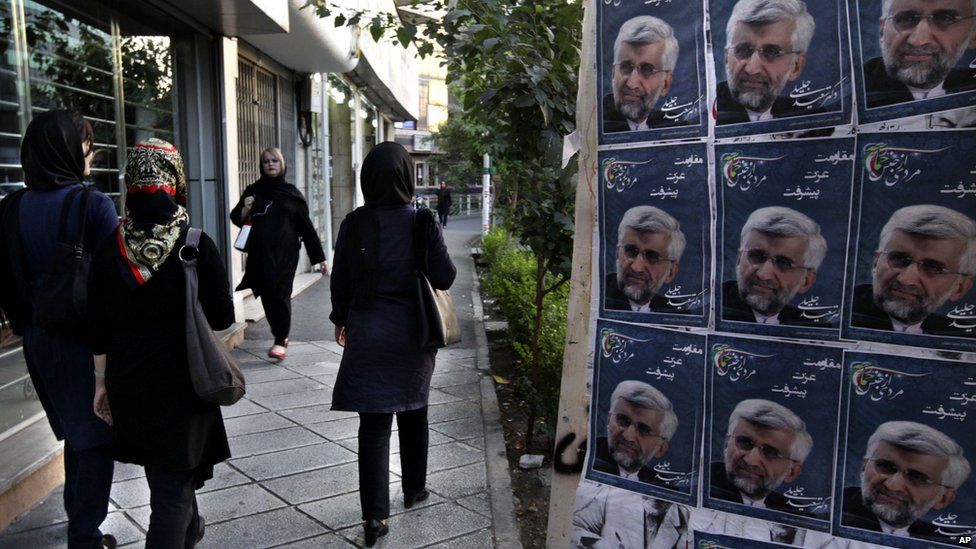 Iranian women walk past photos of conservative presidential candidate, Saeed Jalili, the country's top nuclear negotiator