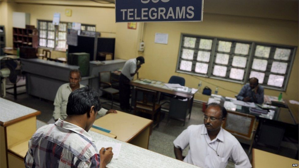 A customer (foreground L) fills in a form for sending out a message using the telegraphic service at a telecommunications office in Bangalore