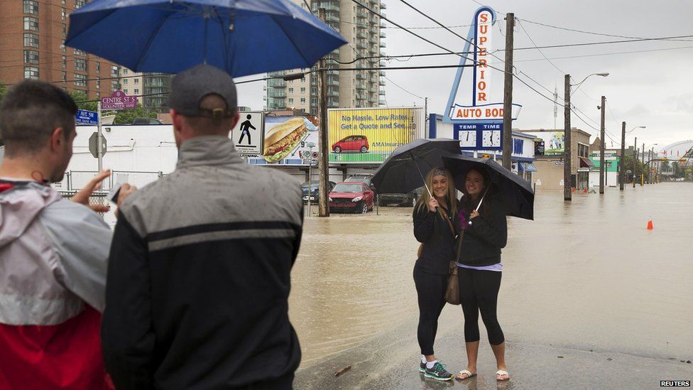 Women pose for a photo as floodwaters rise at a downtown street while evacuating during a mandatory evacuation in Calgary, Alberta June 21, 2013. The heaviest floods in decades shut down the Canadian oil capital, closing roads and bringing down bridges