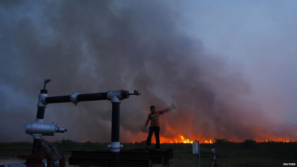 A villager stands on an oil well as fire burns a palm-oil plantation in haze-hit Bangko Pusako district in Rokan Hilir, Indonesia's Riau province, June 22