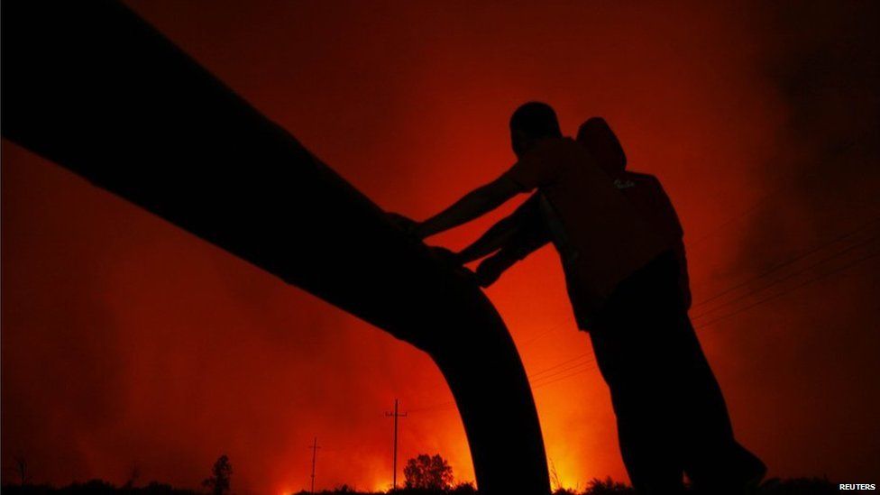 Villagers standing beside on an oil pipe are silhouetted by flames burning a palm-oil plantation in Bangko Pusako district, Riau province, June 22