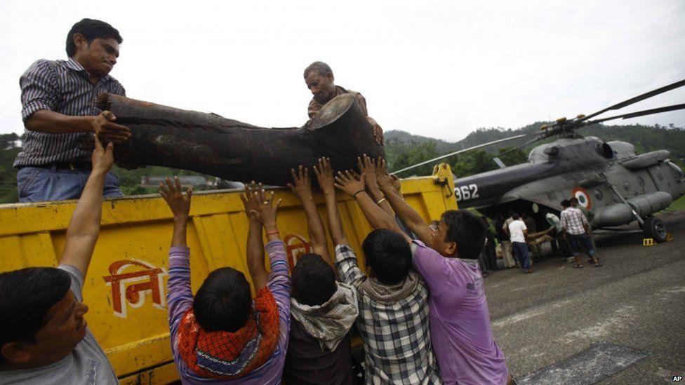 Locals unload a piece of wood from a truck to be placed on to an Indian Air force helicopter as cremation efforts for those killed in landslides and monsoon floods get underway, in Gauchar, Uttarakhand