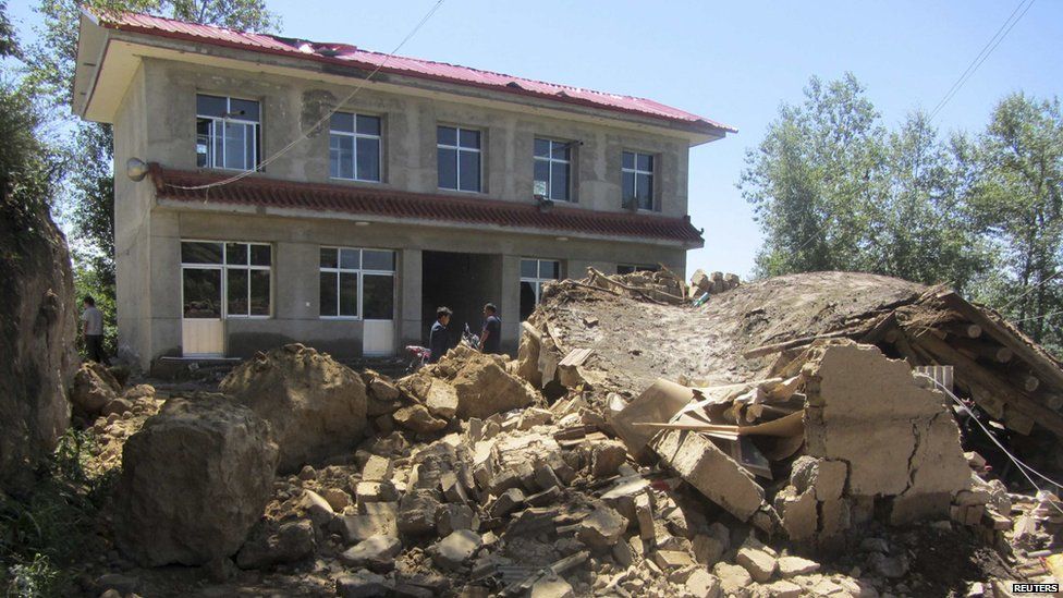 People stand next to a collapsed house after an earthquake struck Minxian county in China's north-west Gansu province on 22 July, 2013.