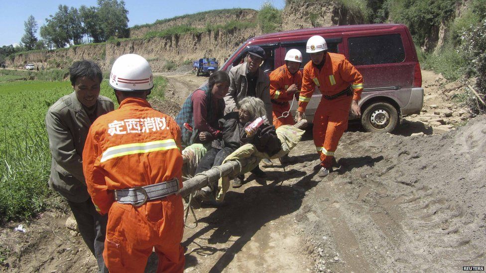 Firefighters carry an injured person along a dirt track on a stretcher after an earthquake hit Minxian county in China's north-west Gansu province on 22 July, 2013.