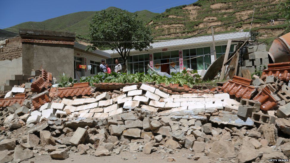 People look at a collapsed wall after an earthquake struck Hetuo township in China's north-west Gansu province on 22 July, 2013.
