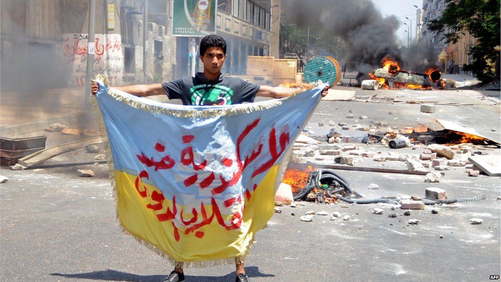 A supporter of the Muslim Brotherhood and Egypt's ousted president Mohammed Morsi holds a banner reading in Arabic "Alexandria is against the coup" as protestors set fire to a council building in Egypt's northern coastal city of Alexandria on 14 August 2013