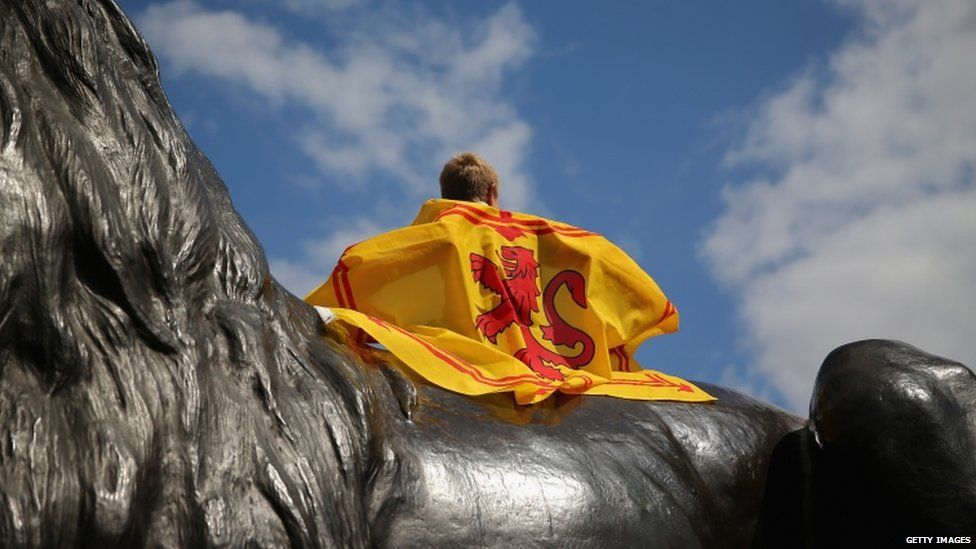 A Scotland fan sits on a statue in Trafalgar Square