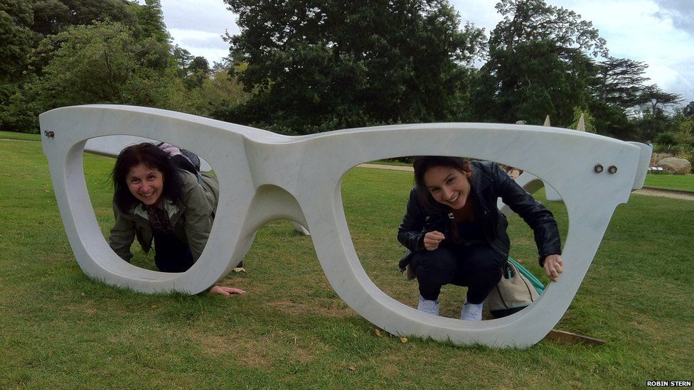 Two women pose inside an sculpture of a pair of glasses