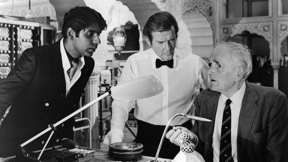 Vijay Amritraj and Roger Moore looking at new gadget that Desmond Llewelyn has created in a scene from the film 'Octopussy', 1983.
