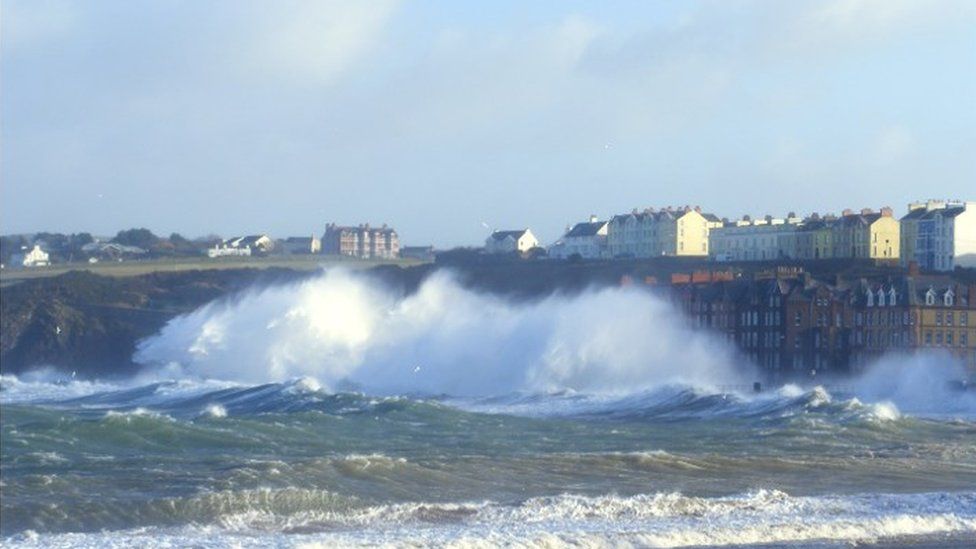 Huge waves crash against land. Tall houses disappear in the spray.