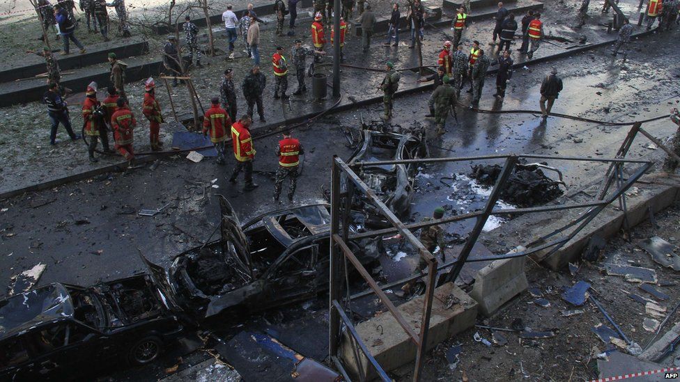 Firemen and onlookers gather around burnt cars at the scene of a huge blast that rocked central Beirut on December 27, 2013
