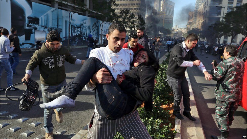 A Lebanese man carries an injured woman at the scene of an explosion in Beirut, Lebanon, (Dec. 27, 2013)