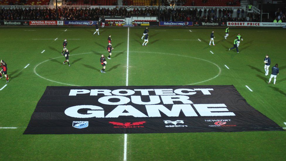 Dragons and Blues players warm up before their match after a protest banner is placed on the pitch