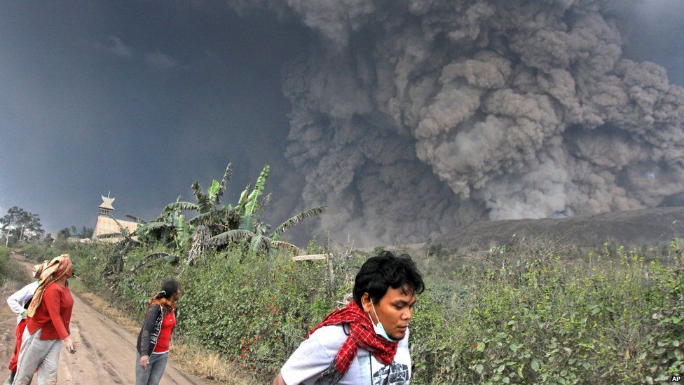 Villagers and a journalist prepare to flee as Mount Sinabung releases pyroclastic flows during an eruption in Namantaran, North Sumatra, Indonesia, Saturday, Feb. 1