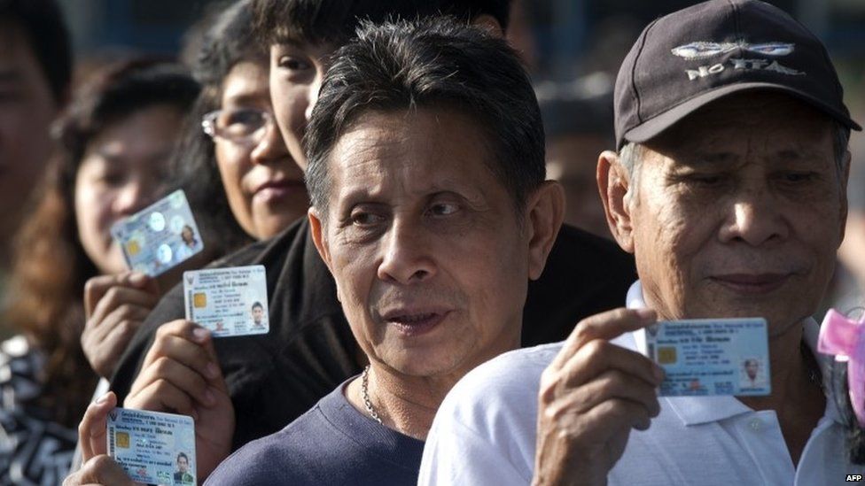 Thai voters show their ID cards as they queue to cast their ballot at a polling station in Bangkok