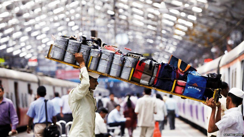 Two porters carry a tray of tiffin boxes onto a train in Mumbai