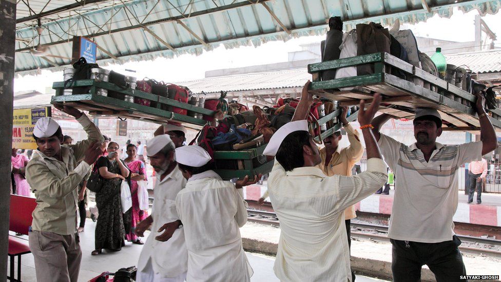 Dabbawalas carrying crates of tiffin tins on their heads.