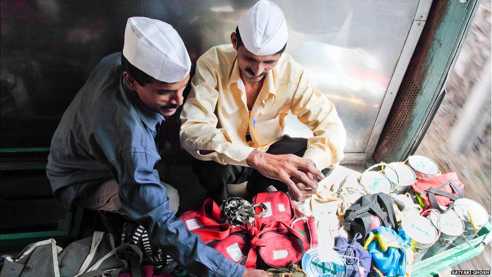 Two Dabbawalas sit on a train checking their tiffin tins.