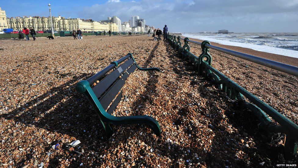 Pebbles blown up from the beach engulf a bench on Hove promenade, in Brighton