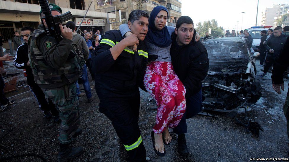 Civil defence members carry a wounded woman as a Lebanese Army soldier secures the area at the site of an explosion in the southern suburbs of Beirut