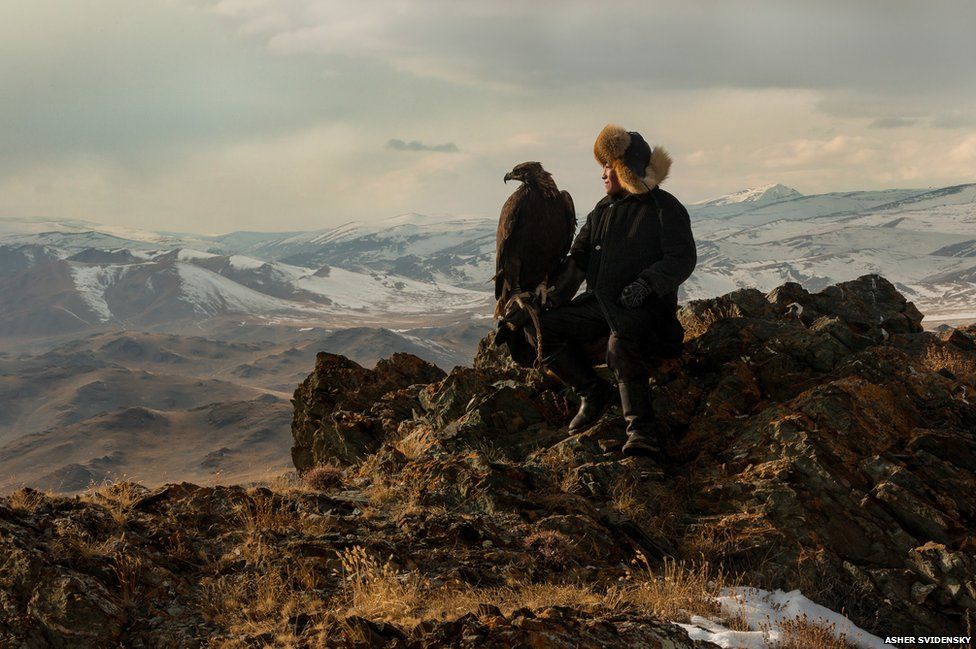 Irka Bolen on a mountain cliff edge with his eagle